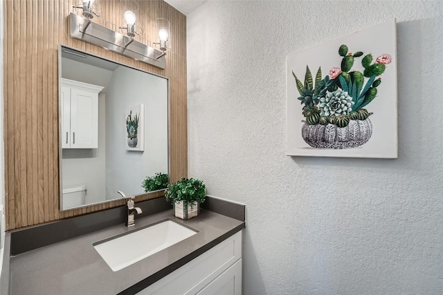 half bathroom with toilet, vanity, and a textured wall