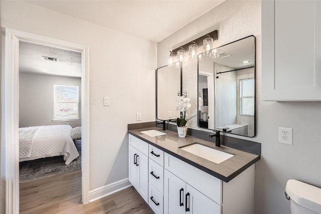 ensuite bathroom with double vanity, toilet, wood finished floors, and a sink