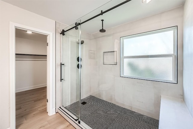 full bathroom featuring a walk in closet, a shower stall, wood finished floors, and baseboards