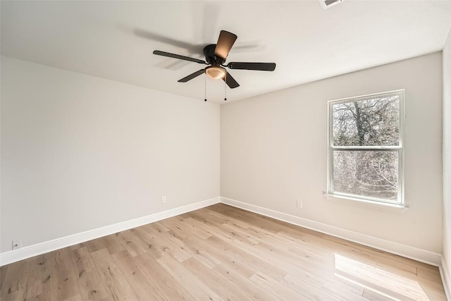 spare room featuring light wood-style flooring, a ceiling fan, and baseboards