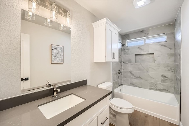 full bath with toilet, wood finished floors,  shower combination, vanity, and a textured wall