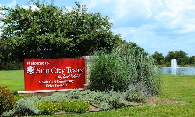 community sign featuring a lawn and a water view