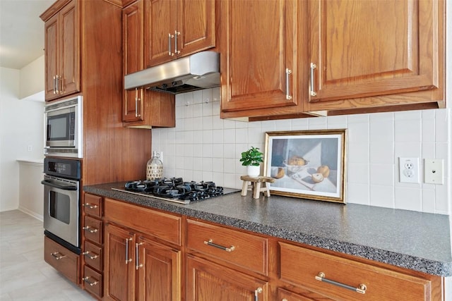 kitchen featuring backsplash, brown cabinets, under cabinet range hood, and stainless steel appliances