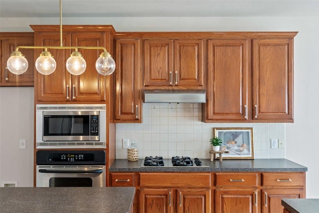 kitchen with dark countertops, appliances with stainless steel finishes, brown cabinetry, and exhaust hood