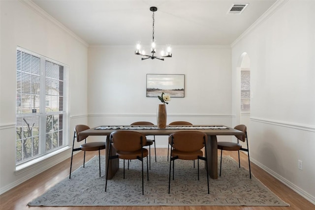 dining area with visible vents, crown molding, wood finished floors, arched walkways, and a notable chandelier