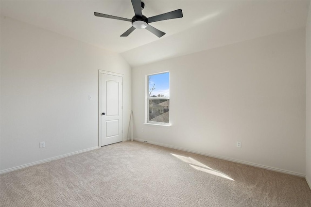 empty room featuring vaulted ceiling, light colored carpet, baseboards, and ceiling fan