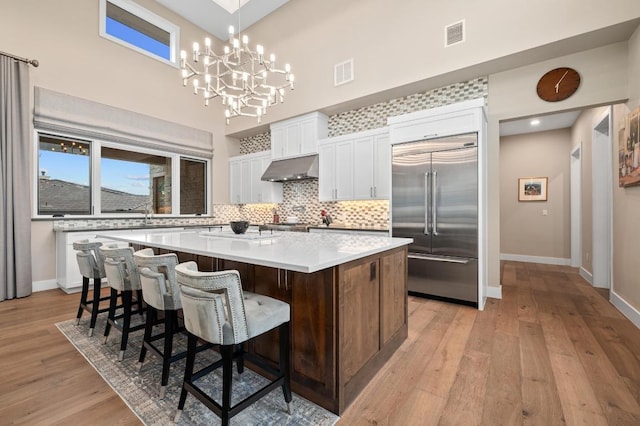 316 Duckhorn Pass, Austin, TX 78738 - kitchen with built in refrigerator, white cabinetry, under cabinet range hood, a large island, and light wood-style floors