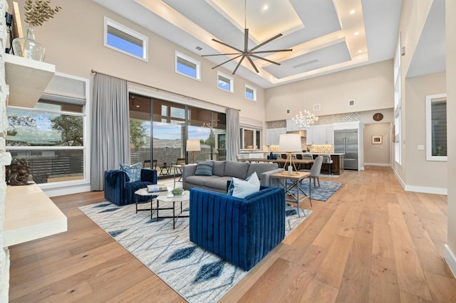 316 Duckhorn Pass, Austin, TX 78738 - living room featuring a towering ceiling, a chandelier, light wood-type flooring, a tray ceiling, and a ceiling fan