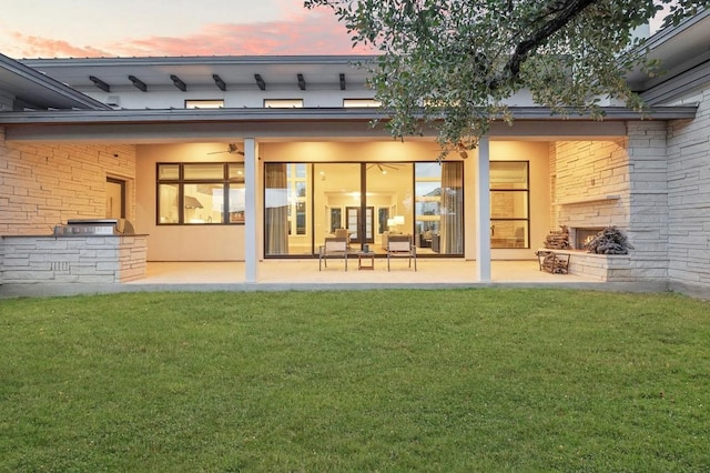316 Duckhorn Pass, Austin, TX 78738 - back of property at dusk featuring a patio area, an outdoor stone fireplace, a yard, brick siding, and ceiling fan