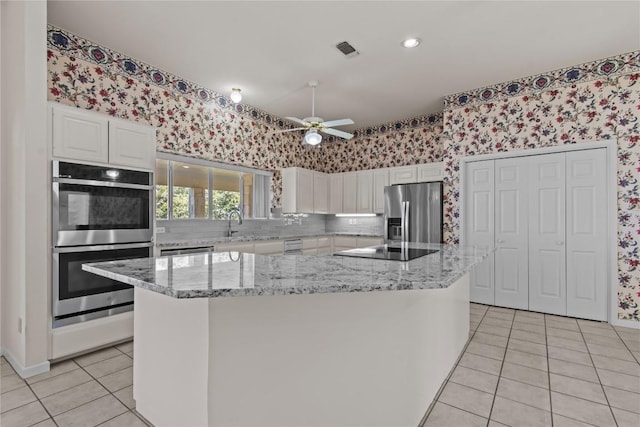 25048 River Rd, Spicewood, TX 78669 - kitchen with appliances with stainless steel finishes, wallpapered walls, light tile patterned floors, white cabinets, and a ceiling fan