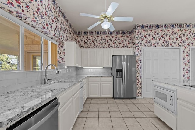 25048 River Rd, Spicewood, TX 78669 - kitchen featuring appliances with stainless steel finishes, wallpapered walls, white cabinetry, backsplash, and light tile patterned floors
