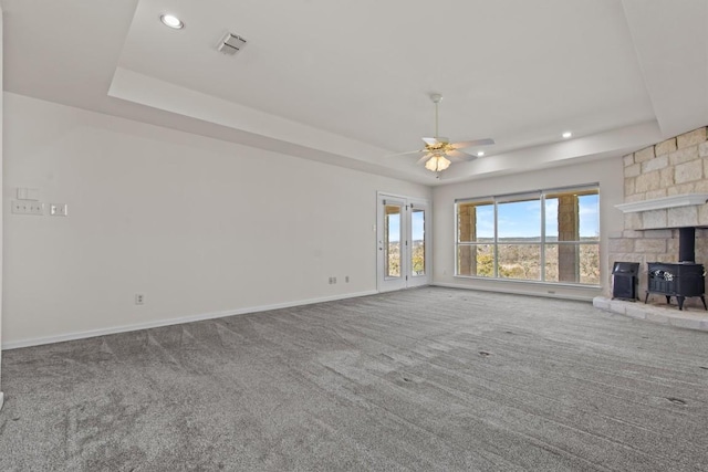 25048 River Rd, Spicewood, TX 78669 - unfurnished living room featuring a tray ceiling, carpet, a ceiling fan, a wood stove, and recessed lighting