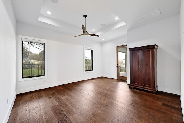 unfurnished bedroom featuring visible vents, baseboards, a raised ceiling, and dark wood-type flooring