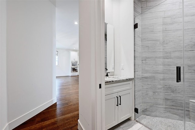 full bathroom featuring a shower stall, vanity, baseboards, and wood finished floors