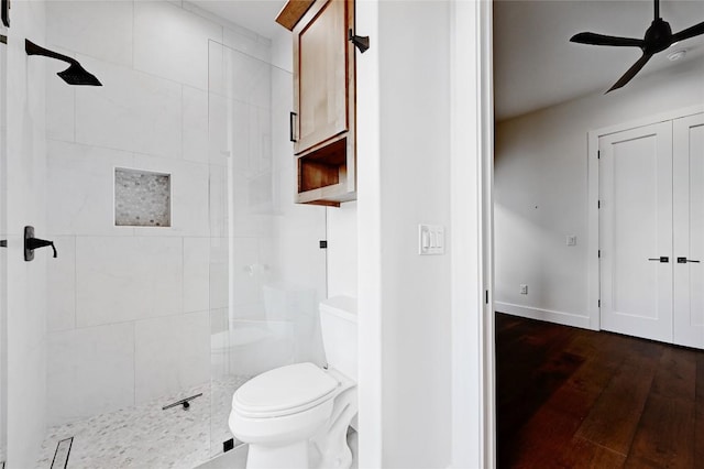 full bath featuring toilet, wood finished floors, a ceiling fan, and a tile shower