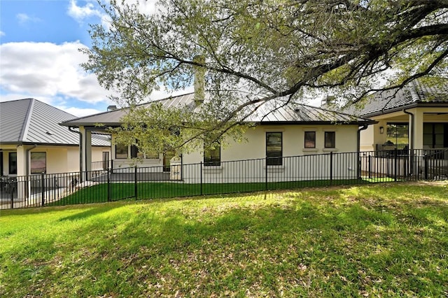 back of property with a lawn, metal roof, fence, and stucco siding