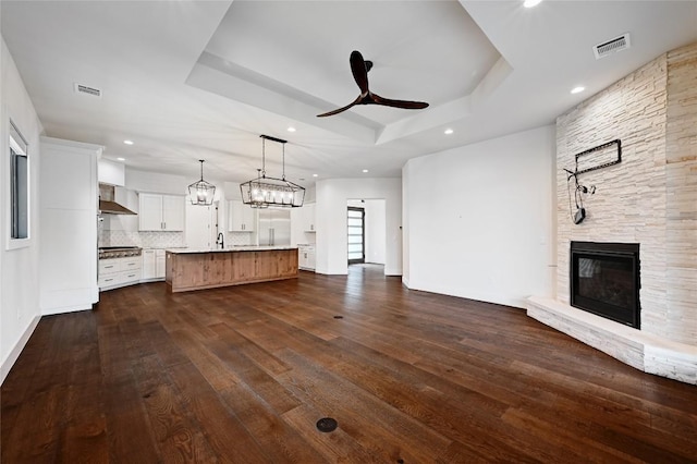 unfurnished living room with visible vents, a stone fireplace, a raised ceiling, and ceiling fan