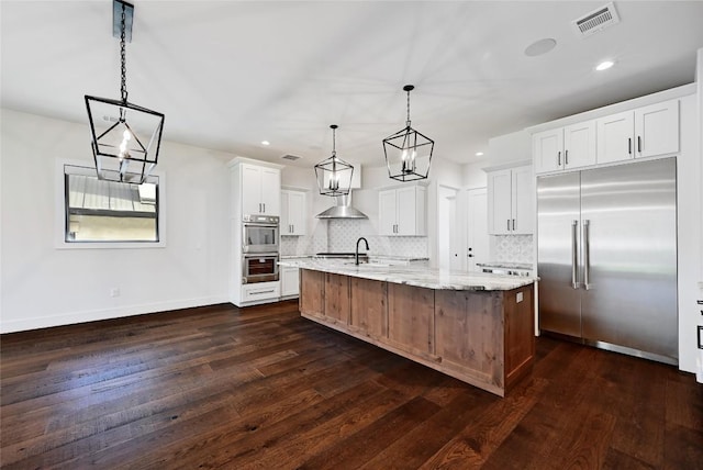 kitchen with visible vents, stainless steel appliances, wall chimney range hood, decorative backsplash, and dark wood-style flooring