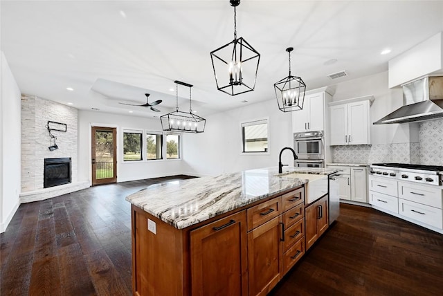 kitchen with ceiling fan with notable chandelier, backsplash, open floor plan, appliances with stainless steel finishes, and wall chimney range hood