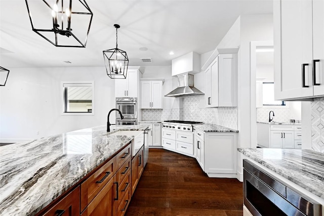 kitchen featuring visible vents, white cabinets, appliances with stainless steel finishes, wall chimney exhaust hood, and a notable chandelier