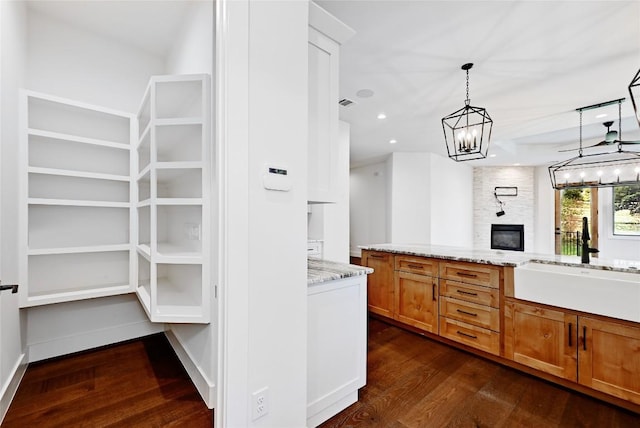 kitchen with pendant lighting, a sink, an inviting chandelier, light stone countertops, and dark wood-style flooring