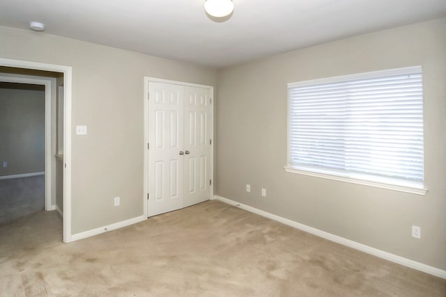 unfurnished bedroom with light carpet, baseboards, and a closet