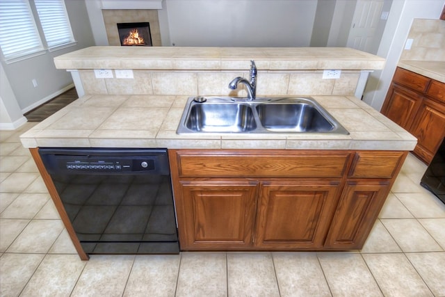 kitchen with light tile patterned floors, brown cabinets, black dishwasher, and a sink