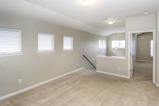 spare room with visible vents, baseboards, light carpet, and vaulted ceiling