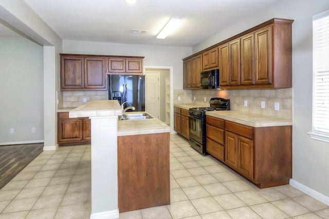 kitchen featuring a kitchen island with sink, black appliances, light countertops, and a sink