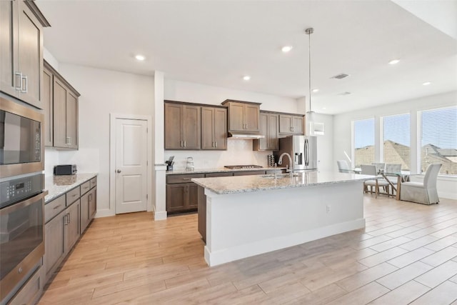 kitchen with visible vents, a center island with sink, light wood-style flooring, stainless steel appliances, and a sink