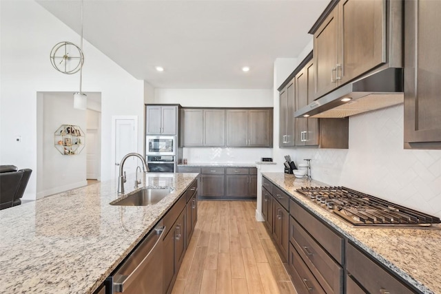 kitchen featuring under cabinet range hood, light stone counters, light wood-style flooring, appliances with stainless steel finishes, and a sink