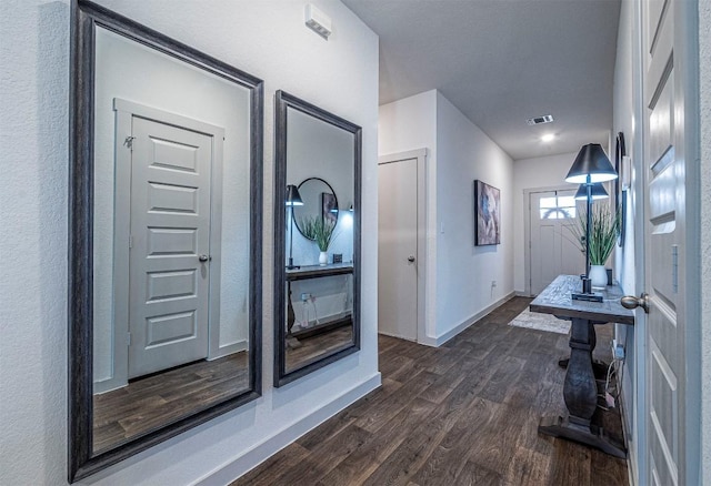 hall with visible vents, baseboards, and dark wood-style floors