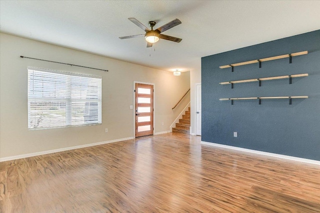 spare room with a ceiling fan, wood finished floors, stairway, and baseboards