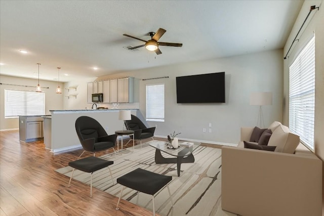 living room with ceiling fan, healthy amount of natural light, light wood-type flooring, baseboards, and recessed lighting
