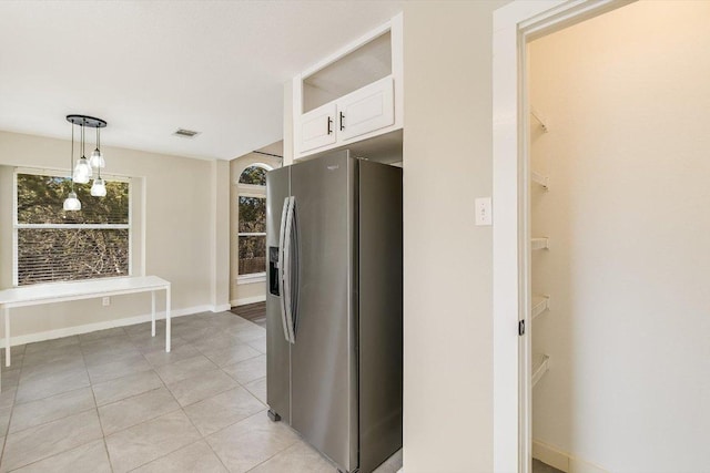 kitchen with light tile patterned floors, baseboards, stainless steel fridge with ice dispenser, white cabinetry, and decorative light fixtures