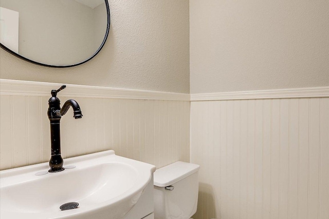 half bath with toilet, a wainscoted wall, and a sink