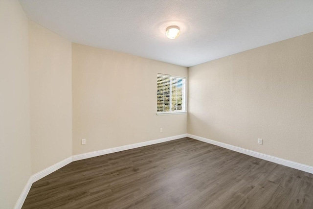 spare room with baseboards and dark wood finished floors