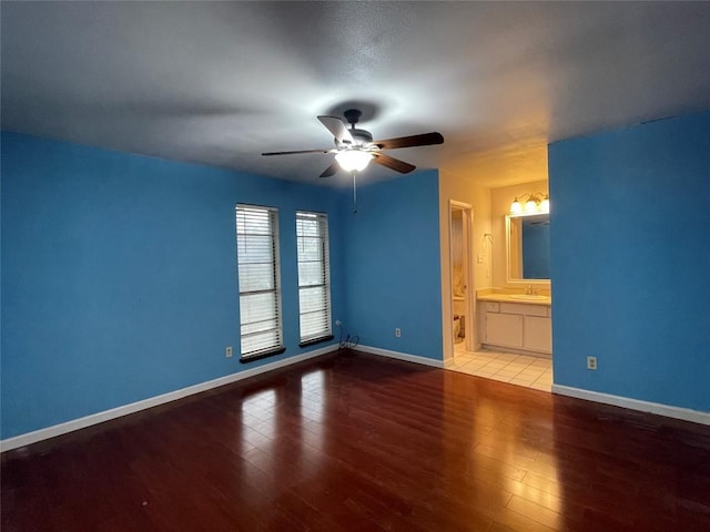 unfurnished bedroom with a ceiling fan, wood finished floors, baseboards, a sink, and ensuite bathroom