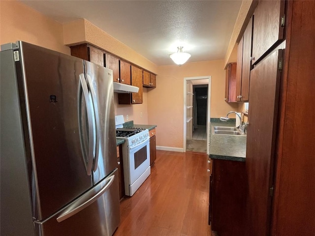 kitchen with white range with gas cooktop, freestanding refrigerator, a sink, dark countertops, and light wood-type flooring