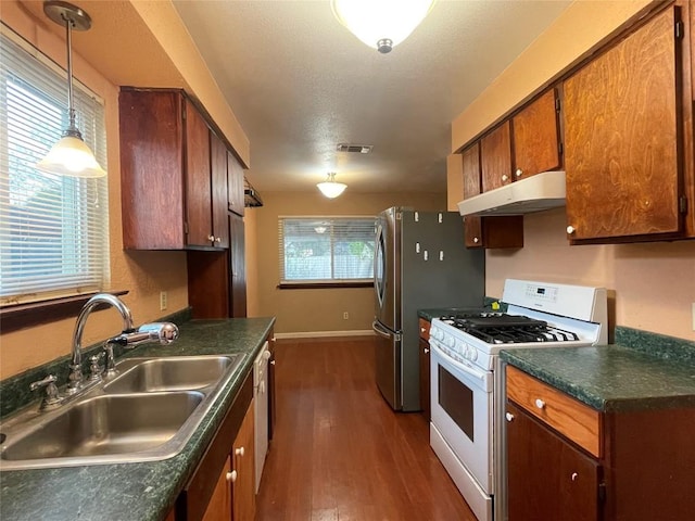 kitchen with dark countertops, visible vents, under cabinet range hood, white gas range, and a sink