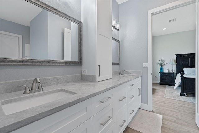 ensuite bathroom with visible vents, ensuite bathroom, a sink, wood finished floors, and double vanity