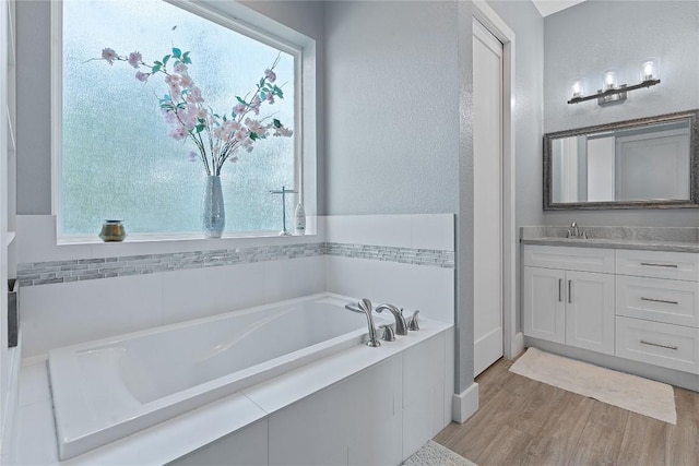 full bath with a healthy amount of sunlight, wood finished floors, vanity, and a bath