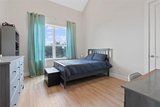 bedroom with light wood finished floors, baseboards, and lofted ceiling