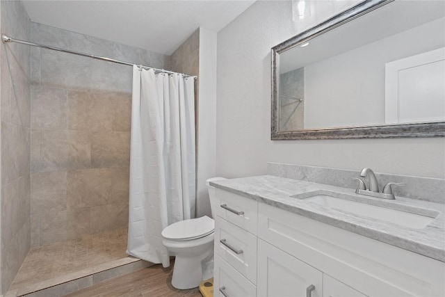 bathroom featuring toilet, wood finished floors, vanity, and a tile shower