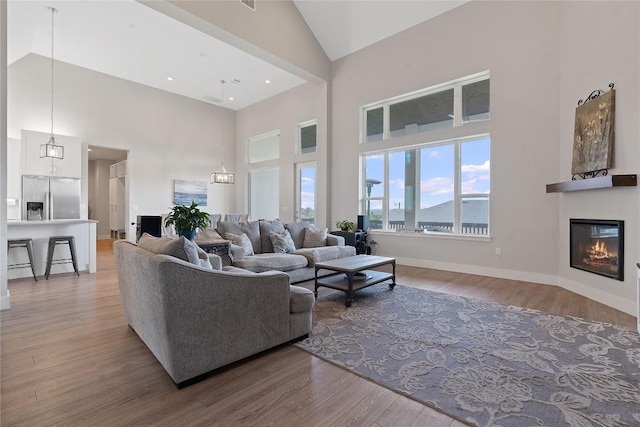 living room with a glass covered fireplace, baseboards, light wood finished floors, and high vaulted ceiling