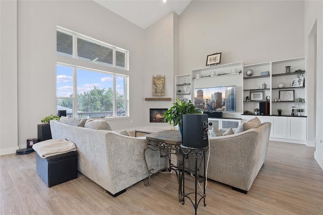 living area featuring a glass covered fireplace, light wood-style flooring, and high vaulted ceiling