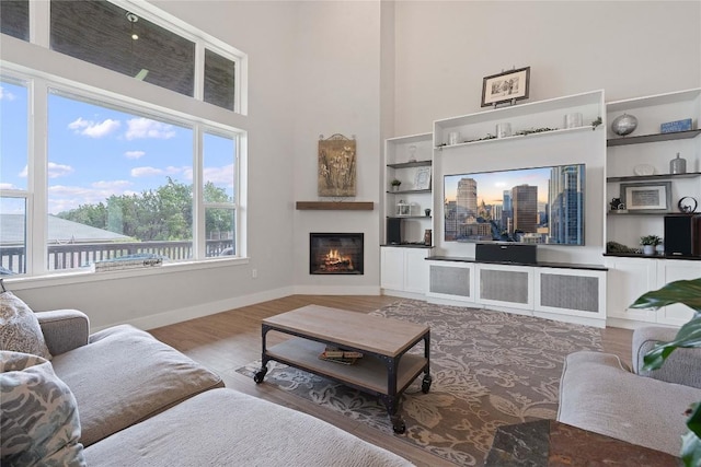 living area featuring built in features, wood finished floors, baseboards, a high ceiling, and a lit fireplace