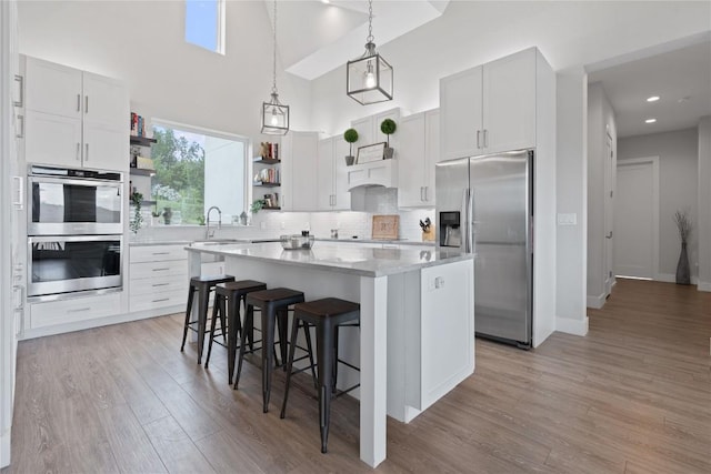 kitchen featuring a breakfast bar, open shelves, a center island, stainless steel appliances, and light wood-style floors