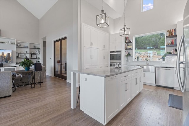 kitchen featuring light wood finished floors, open shelves, appliances with stainless steel finishes, french doors, and a sink