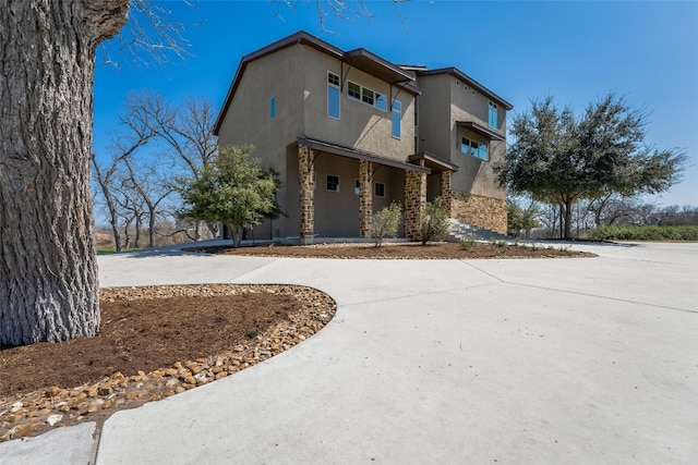 view of front facade featuring stone siding, stucco siding, and concrete driveway